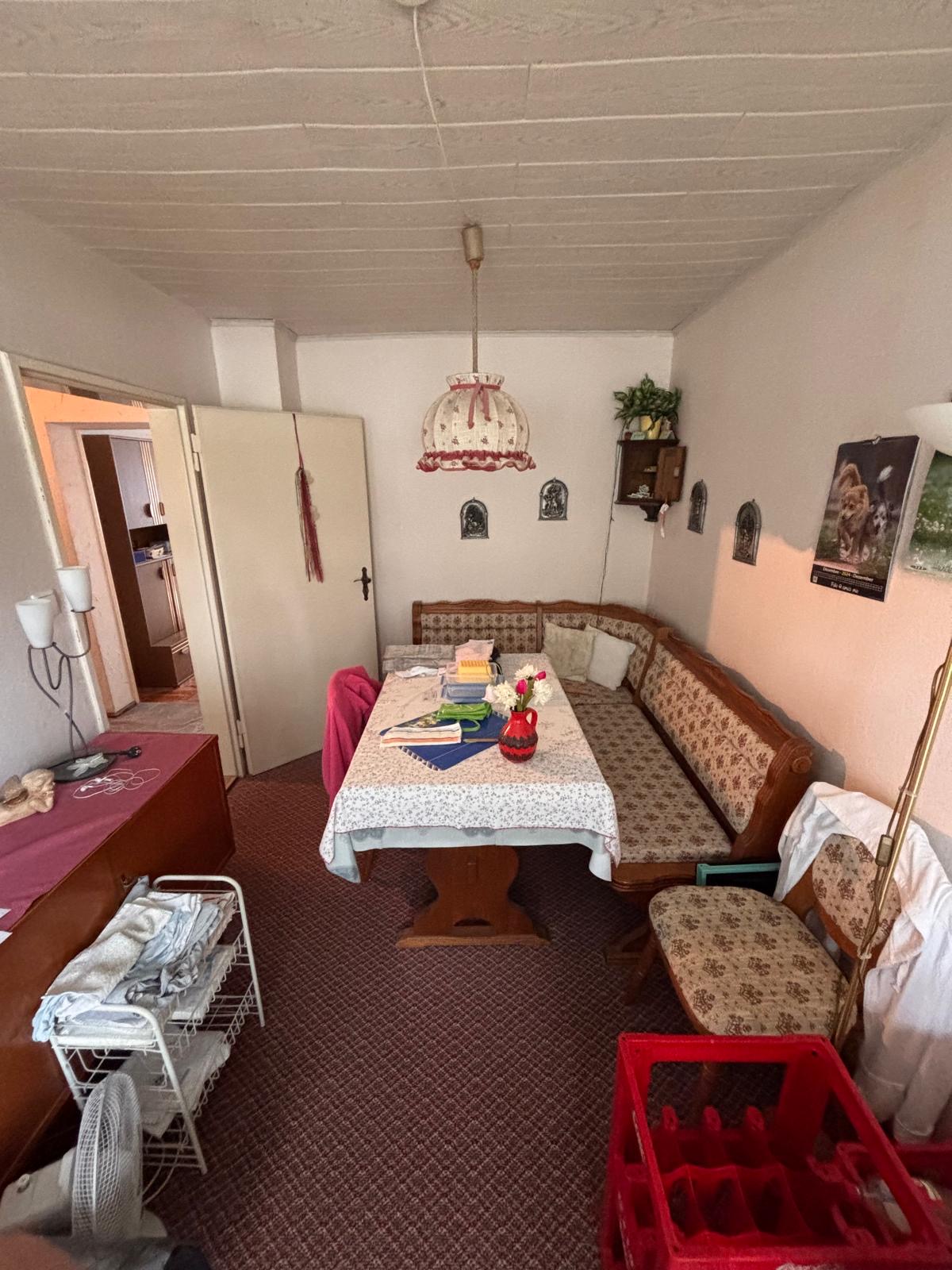 Kleine, gemütliche Stube mit Tisch, Stühlen und einer wärmeren Farbpalette.