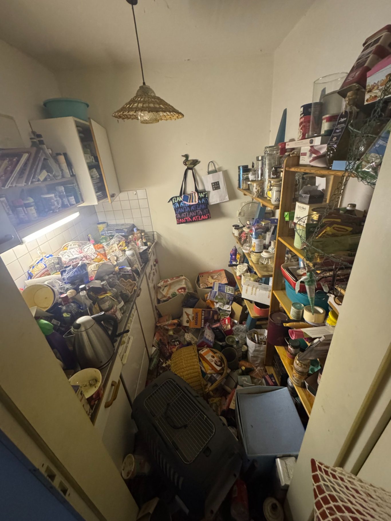 Unordentliche Küche mit überfüllten Regalen und verstreuten Gegenständen auf dem Boden.