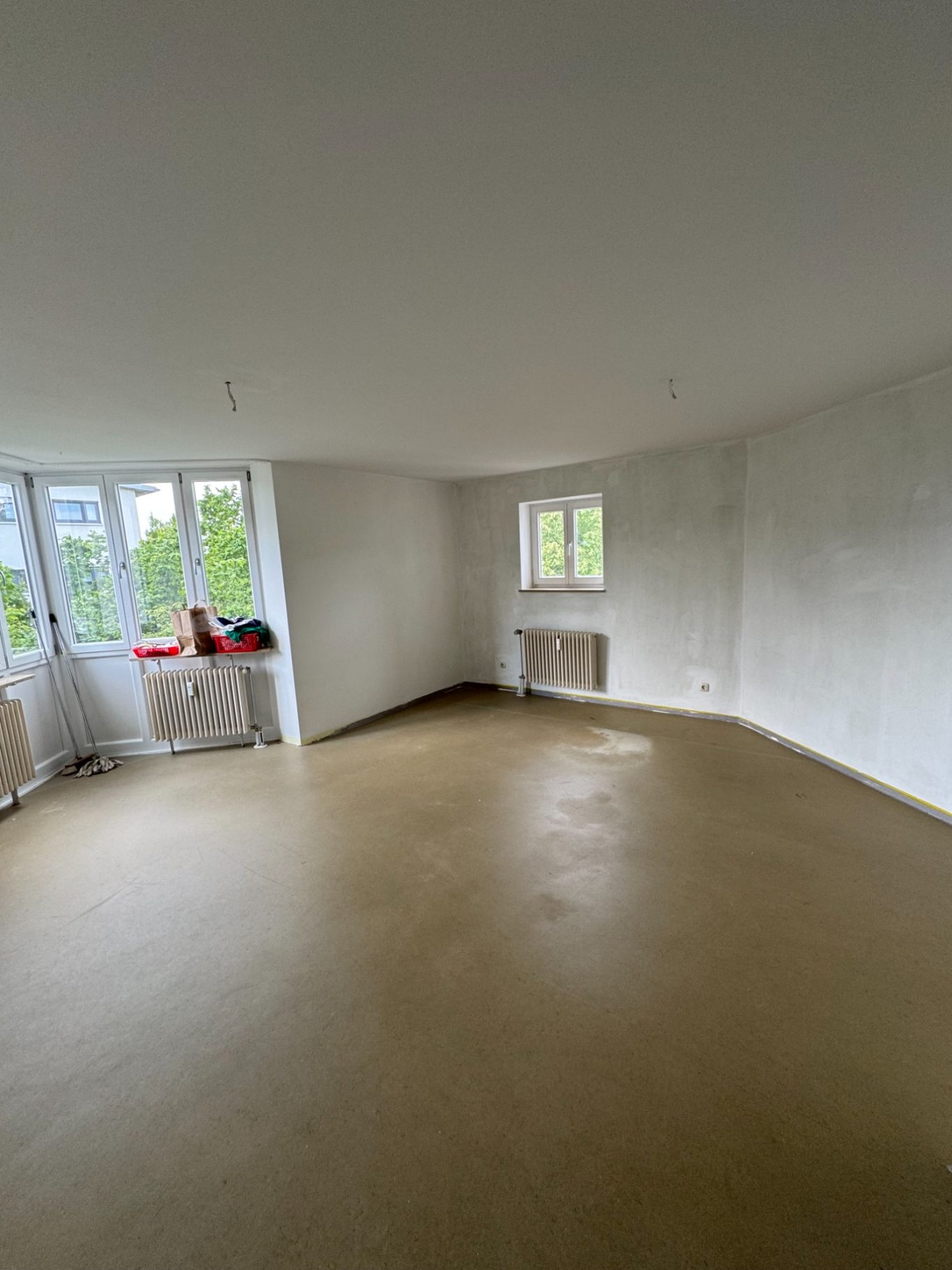 Leeres, helles Zimmer mit großen Fenstern und neutralen Wänden.