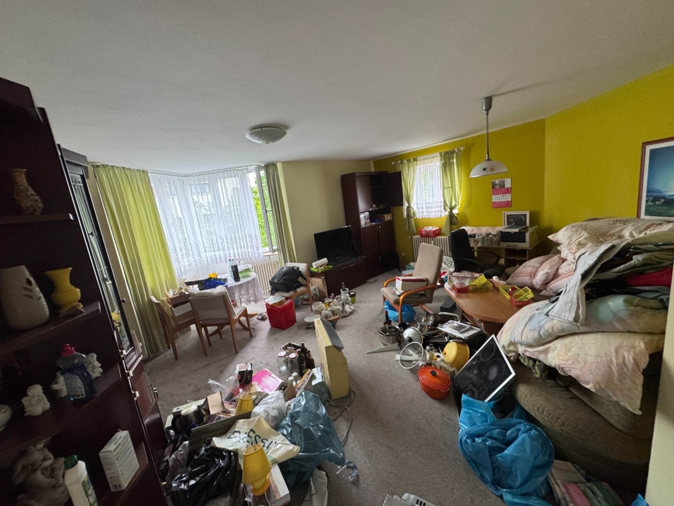 Unordentliches Wohnzimmer mit verstreuten Möbeln und Kisten in gelber Umgebung.