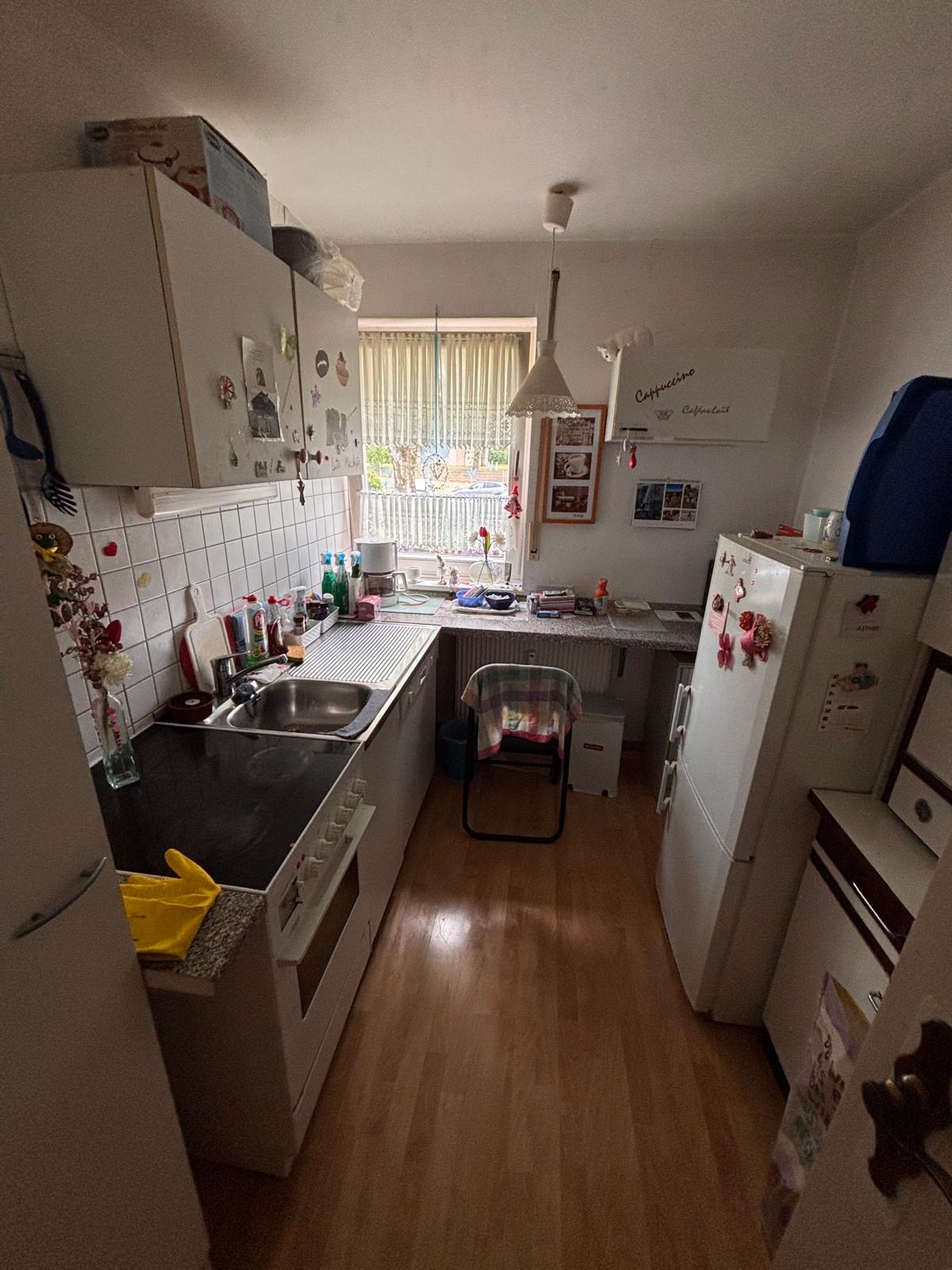 Kleine, helle Küche mit Spüle, Kühlschrank und Fenster, die Tageslicht hereinlässt.